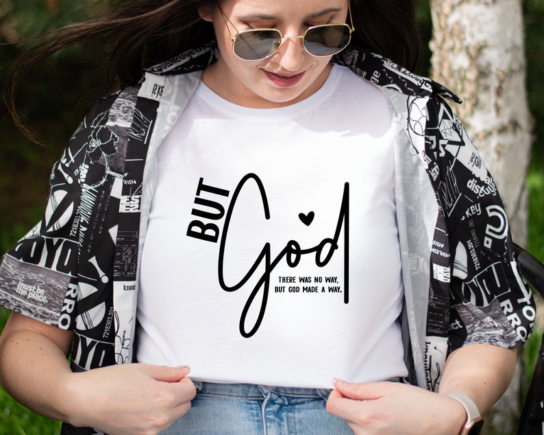 May include: White t-shirt with black text that reads "BUT GOD" in a cursive font. The text "THERE WAS NO WAY, BUT GOD MADE A WAY." is written in a smaller font below the main text.