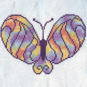 Puede incluir: Un patrón de punto de cruz de una mariposa colorida con tonos de morado, naranja, amarillo y azul.