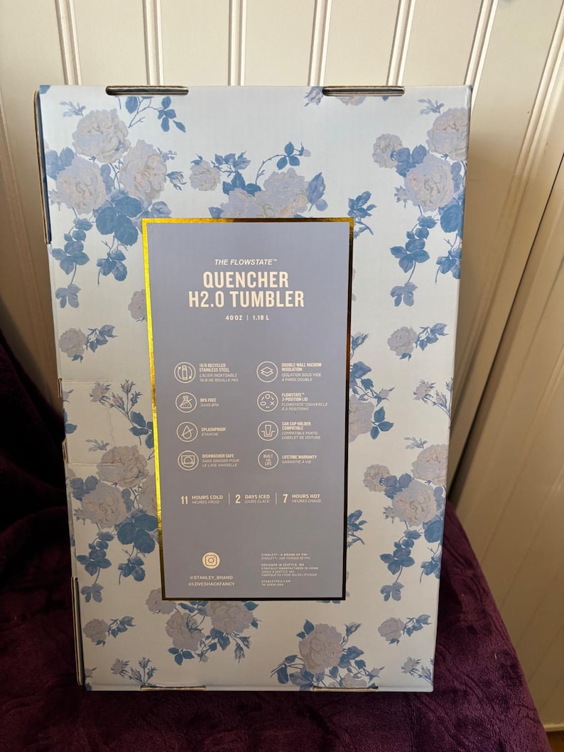 Może przedstawiać: Kartonowe pudełko z kwiatowym wzorem w kolorze jasnoniebieskim i białym. Pudełko zawiera "QUENCHER H2.0 TUMBLER". Pudełko ma złote obramowanie wok&oacute;ł etykiety ze szczeg&oacute;łami produktu. Pudełko ma 1,18 L.
