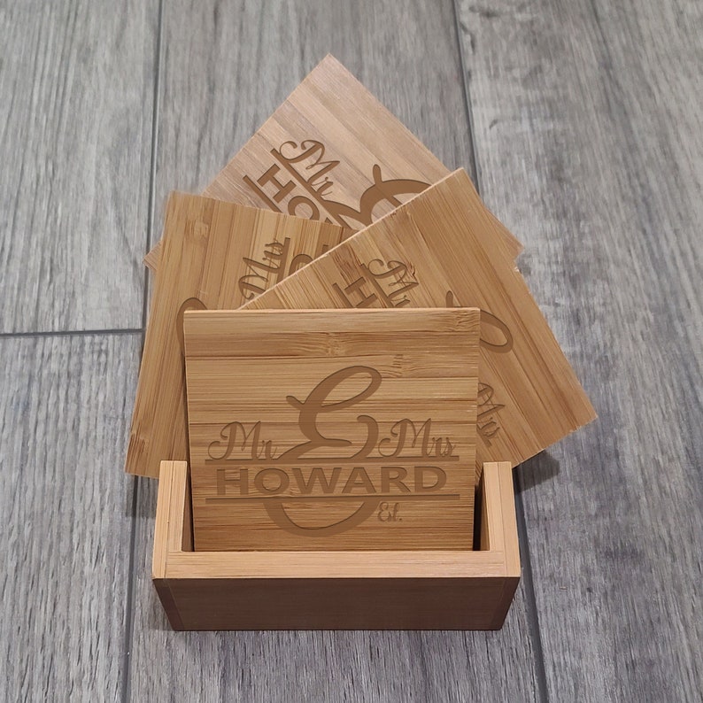 May include: Set of four bamboo coasters with a holder. The coasters are engraved with "Mr. & Mrs. HOWARD Est." and a stylised letter "G".
