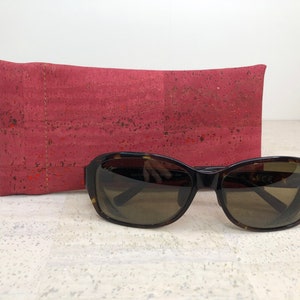 May include: A red cork sunglasses case with a pair of brown tortoise shell sunglasses.