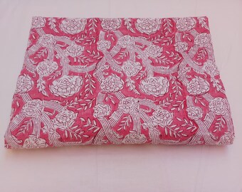 May include: A pink cotton fabric with a white floral pattern. The fabric is folded in half and has a textured surface.