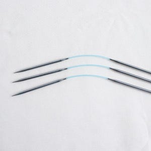 May include: Four silver knitting needles with blue cords. The needles are arranged in a curved pattern.