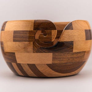 May include: A wooden yarn bowl with a unique spiral design. The bowl is made from different types of wood, creating a patchwork pattern.
