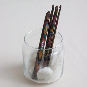 May include: Three wooden crochet hooks in a glass jar with white cotton wool balls. The hooks are multi-coloured and have the sizes 12.0mm, 8.0mm, and 6.0mm printed on them.