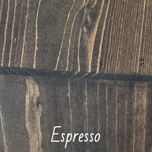 May include: A white ceramic mug with a black handle and the text "But First, Coffee" in a handwritten style. The mug is on a white surface. The mug is approximately 10 cm tall.