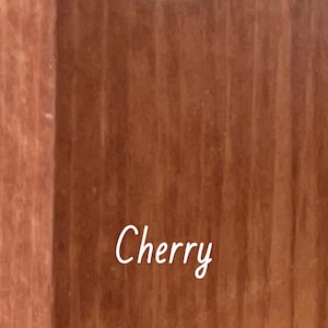 May include: A white ceramic mug with a black handle and the text "But First, Coffee" in a bold, black font. The mug is on a wooden surface. The mug is approximately 10 cm tall.