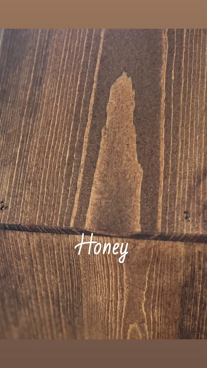May include: Close-up of a wooden surface with a warm honey-coloured stain. The wood grain is visible, with vertical lines and a lighter, irregular shape in the centre. The word "Honey" is written in cursive.