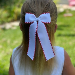 May include: A white bow with a red scalloped edge. The bow is tied in a ponytail.