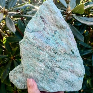 May include: A large, rough-cut mineral specimen featuring a vibrant turquoise and mint green colour palette with visible crystalline textures, natural striations, and subtle dark brown mineral inclusions throughout the jagged, triangular stone surface.