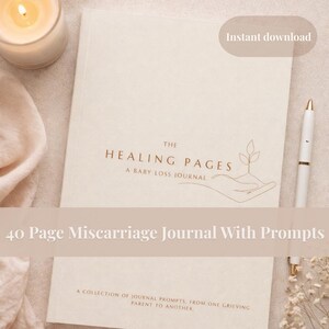 Op de afbeelding: Een beige dagboek getiteld "The Healing Pages: A Baby Loss Journal" met de tekst "40 Page Miscarriage Journal With Prompts". Een witte pen en een brandende kaars liggen naast het dagboek. Het dagboek heeft een lijntekening van een hand die een plant vasthoudt.