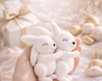May include: Two white plush bunny toys with closed eyes are held in a hand. The bunnies are hugging each other. The image has text that reads "DIY Bunny Pattern" and "Instant Download". A PDF pattern is also advertised.