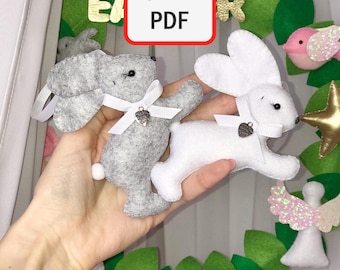 May include: Two felt bunny ornaments, one gray and one white, with white satin bows and silver heart charms. The bunnies are hanging on a green felt wreath with pink and white felt eggs, a pink bird, and a gold star.