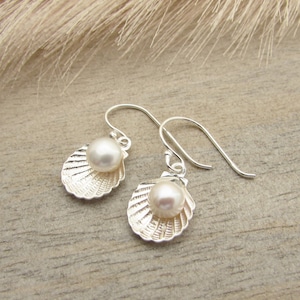 May include: A pair of silver earrings with a pearl in each shell-shaped pendant.