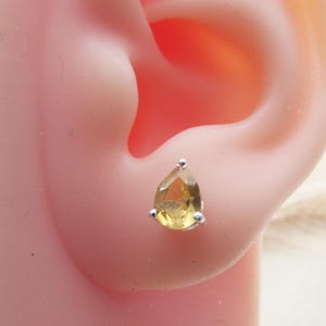 May include: A pair of silver teardrop earrings with a yellow gemstone.