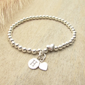 May include: Silver beaded bracelet with a heart charm and a charm with the letter H.