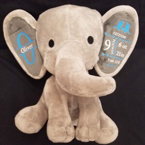 May include: Grey plush elephant soft toy with blue embroidered details. One ear says "Oliver" and the other ear says "9 pounds 6 oz, 21 in, 7:46 AM, 12/27/19".