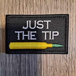 May include: Black patch with white text that reads "Just the Tip" and a yellow and green bullet underneath.