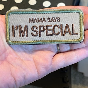 May include: A gray fabric patch with a green border. The patch has brown embroidered text that reads "Mama Says I'm Special."