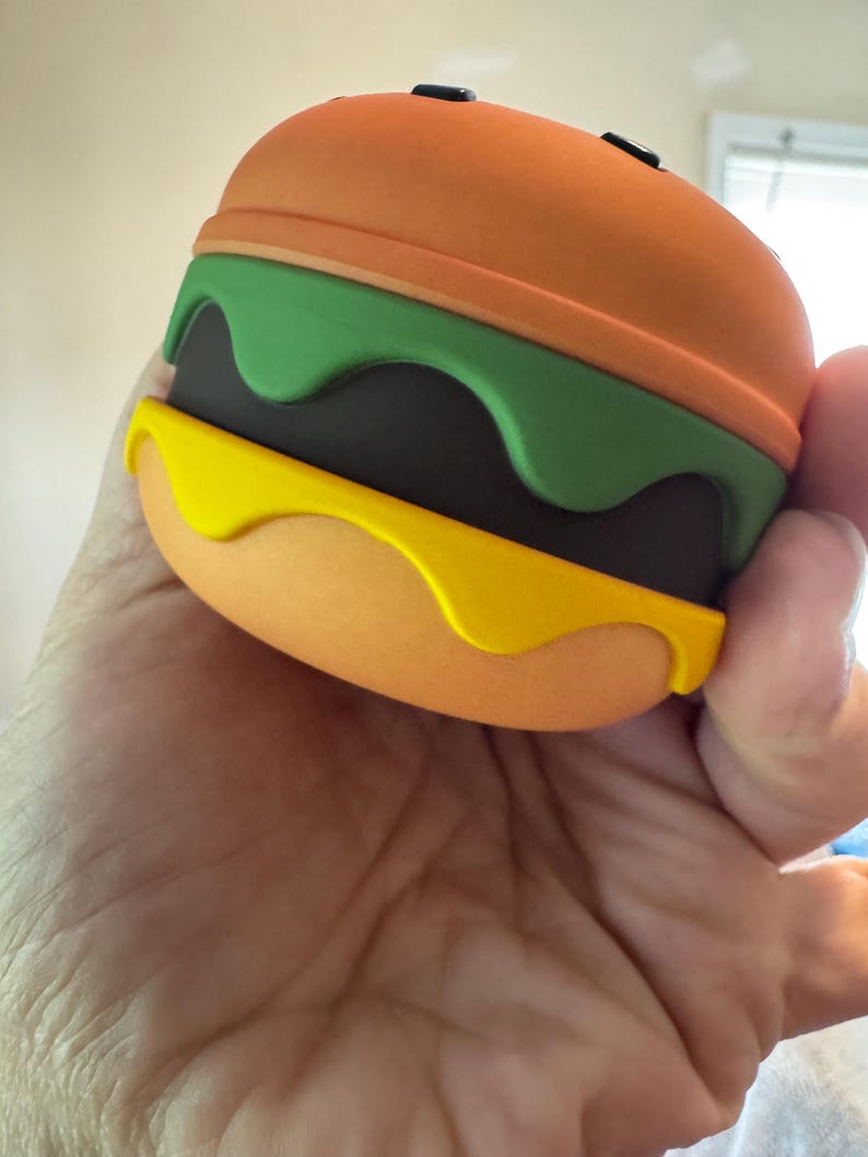 May include: A novelty burger-shaped object with orange, green, yellow, and brown layers. The top and bottom buns are orange, with a green layer resembling lettuce, a brown patty, and yellow sauce.