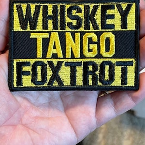 May include: A black and yellow embroidered patch with the text "Whiskey Tango Foxtrot".