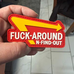 May include: A red and yellow patch with the text "FUCK-AROUND N-FIND-OUT" in white block letters. The patch has a yellow arrow design and a red border.