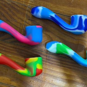 May include: Four silicone smoking pipes with curved stems and bowls. Each pipe features a unique marbled color pattern: one is pink and blue, one is blue and white, one is red, yellow, and green, and one is blue, green, and white.