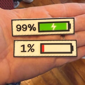 May include: Two rectangular patches with black borders. One reads "99%" with a green battery graphic and lightning bolt. The other reads "1%" with a red battery graphic. Both have a white background.