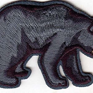 May include: Embroidered iron-on patch of a black bear walking to the right. The bear is gray with a dark purple outline and a yellow nose.