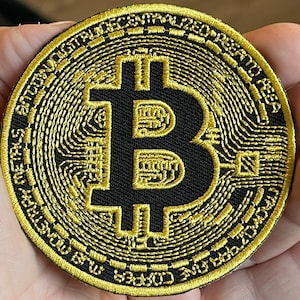 May include: A gold embroidered patch with a black background featuring the Bitcoin symbol and the text "Bitcoin Decentralized Peer to Peer", surrounded by a circular design.