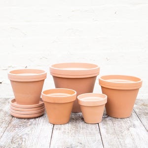 May include: Five terracotta pots of varying sizes, with the largest pot in the centre. The pots are arranged on a wooden surface.
