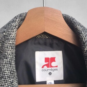 May include: A black and white tweed jacket hanging on a wooden hanger. The jacket has a black lining and a label with the Courr&egrave;ges logo in red and the number 21. The size tag reads 38.