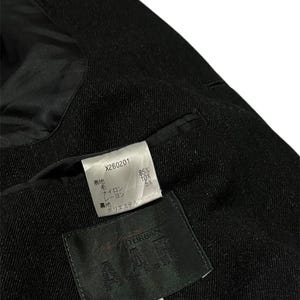 K&ouml;nnte beinhalten: Nahaufnahme eines schwarzen Blazers mit strukturiertem Stoff. Das Innenfutter ist schwarz und gl&auml;nzend. Zwei Etiketten sind sichtbar, eines mit dem Text "X260201" und Materialprozenten, und ein weiteres mit dem Markennamen "DURBAN" und der Gr&ouml;&szlig;e "M".