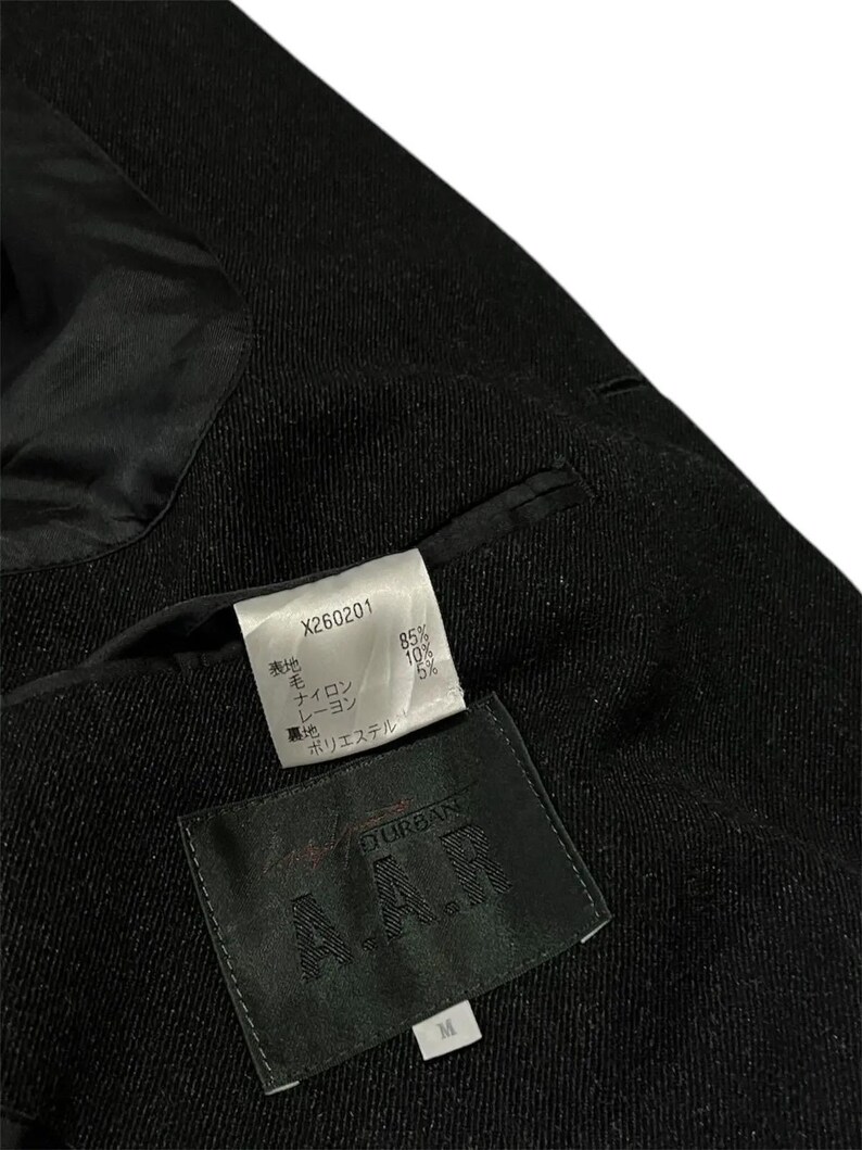 K&ouml;nnte beinhalten: Nahaufnahme eines schwarzen Blazers mit strukturiertem Stoff. Das Innenfutter ist schwarz und gl&auml;nzend. Zwei Etiketten sind sichtbar, eines mit dem Text "X260201" und Materialprozenten, und ein weiteres mit dem Markennamen "DURBAN" und der Gr&ouml;&szlig;e "M".