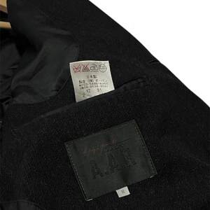 K&ouml;nnte beinhalten: Nahaufnahme des Innenraums einer schwarzen Wolljacke. Das Futter ist schwarz, und ein Etikett mit dem Text "A.A.R" ist sichtbar. Ein kleineres Etikett mit japanischem Text und Pflegesymbolen ist ebenfalls vorhanden. Die Jacke scheint Gr&ouml;&szlig;e M zu haben.