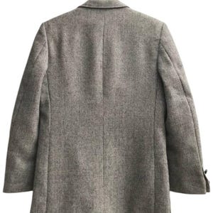 May include: A tweed blazer in a neutral color palette hangs on a wooden hanger. The jacket features a classic notched lapel, two buttons on the sleeves, and a tailored fit. The fabric has a subtle textured pattern.