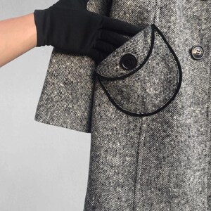 May include: A black and white tweed coat with a rounded pocket and black trim. The coat has large black buttons and a classic design. The sleeve is short and the fabric has a speckled pattern.