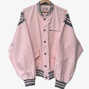 Puede incluir: Chaqueta bomber rosa claro con rayas grises en las mangas y pu&ntilde;os. La chaqueta tiene cierre de botones, un peque&ntilde;o bolsillo con cremallera y la palabra "STUFF" en la etiqueta.