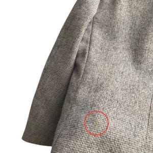May include: Close-up of a gray blazer with a subtle houndstooth pattern. The fabric appears to be a woven material, with a visible sleeve and shoulder. A small stain is visible on the blazer.