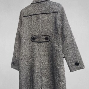 May include: A gray tweed coat with black trim and buttons. The coat is hanging on a wooden hanger. The coat has a classic design with a notched collar and two rows of buttons. The coat is made of a textured fabric.