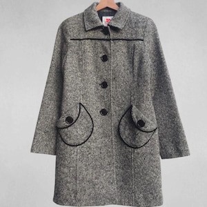May include: A gray tweed coat with black trim and buttons. The coat has a classic design with a collar, long sleeves, and two decorative pockets. The coat is hanging on a wooden hanger.