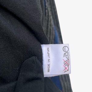 May include: Close-up of a black fabric with a blue stripe and a white tag. The tag reads "MADE IN JAPAN" in black text. Washing instructions are also printed on the tag.