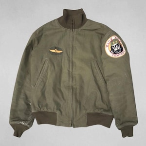 May include: Olive green bomber jacket with a high collar, ribbed cuffs, and hem. Features a patch on the left chest with a gold wing design and a larger patch on the right sleeve with a gorilla graphic and the text "King Army Company".