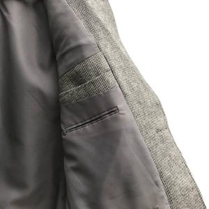 May include: Close-up of the inside of a gray tweed blazer. The interior features a smooth, gray lining with two pockets. The blazer is hanging on a wooden hanger, showcasing the tailored construction and quality of the garment.