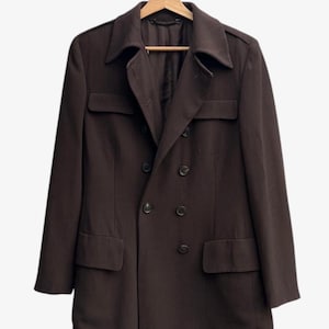 May include: A dark brown double-breasted coat with a notched collar, two front pockets, and four buttons. The coat is hanging on a wooden hanger against a white background. The coat has a classic, tailored design.
