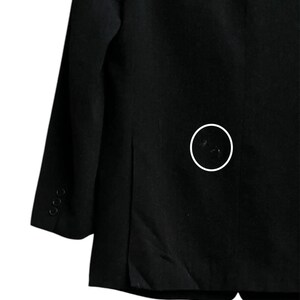 K&ouml;nnte beinhalten: Ein schwarzer Blazer mit fallendem Revers und drei Kn&ouml;pfen am &Auml;rmel. Der Blazer hat ein klassisches Design und ist aus einem einfarbigen, dunklen Stoff gefertigt. Das Bild zeigt eine Nahaufnahme der R&uuml;ckseite des Blazers.