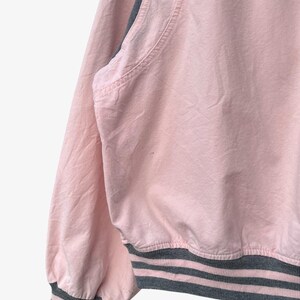 Puede incluir: Chaqueta bomber rosa con dobladillo y pu&ntilde;os de canal&eacute; grises. La chaqueta tiene un dise&ntilde;o cl&aacute;sico con cuello redondo y manga larga. Los pu&ntilde;os y el dobladillo presentan rayas grises.