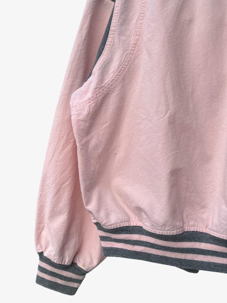 Puede incluir: Chaqueta bomber rosa con dobladillo y pu&ntilde;os de canal&eacute; grises. La chaqueta tiene un dise&ntilde;o cl&aacute;sico con cuello redondo y manga larga. Los pu&ntilde;os y el dobladillo presentan rayas grises.