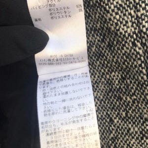 May include: Close-up of a clothing tag with Japanese text and fabric composition details. The tag lists materials like wool, polyester, and nylon. The background is a black and white tweed fabric.