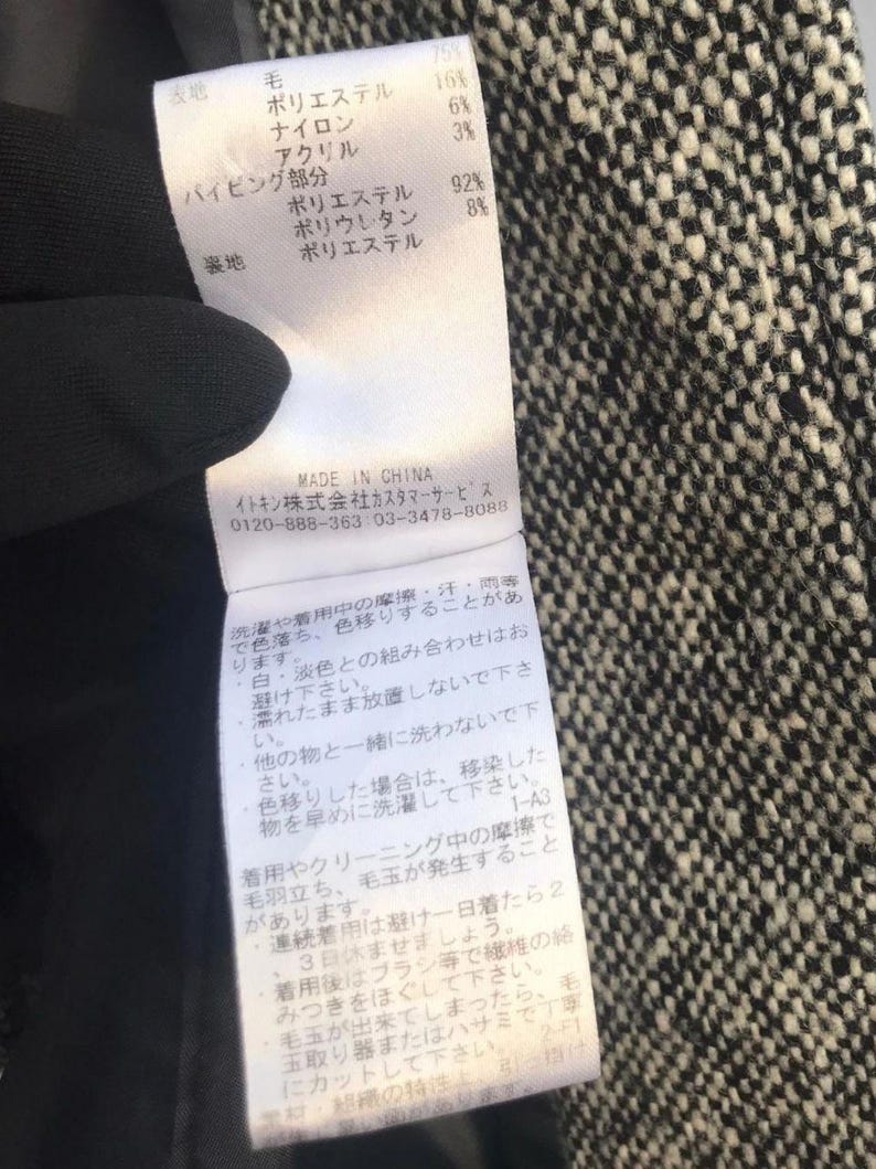May include: Close-up of a clothing tag with Japanese text and fabric composition details. The tag lists materials like wool, polyester, and nylon. The background is a black and white tweed fabric.